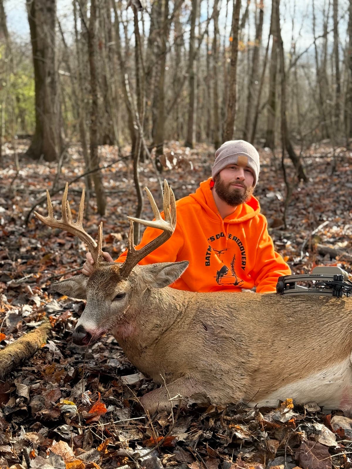 Hunter in blaze orange with a wide-racked buck recovered in the autumn woods